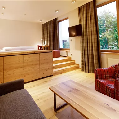 A modern room with wooden floors and large windows. It is furnished with a gray sofa, a red armchair, and a low table.