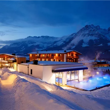 A modern hotel in a snowy mountain landscape at twilight. The outdoor area features a lit pool and snow-covered landscapes.