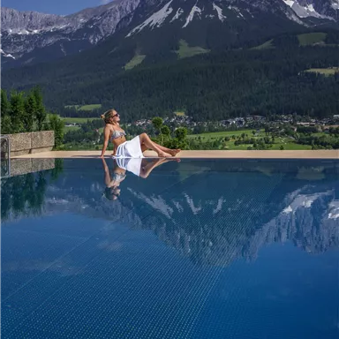 A relaxing pool with a view of majestic mountains. A woman enjoys the scenery in a tranquil setting.