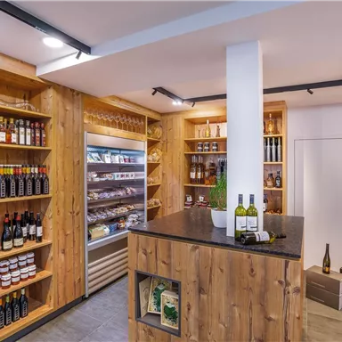 An inviting sales room with wooden shelves full of bottles and gourmet items. In the center, there is a sales counter with some wine bottles.