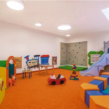 A vibrant playroom for children with colorful toys and a slide. The floor is orange and there are various play stations.
