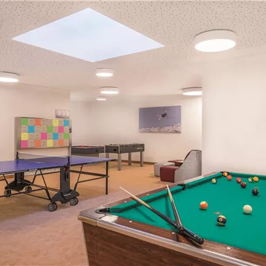 A recreational room with a pool table and a table tennis court. The room has bright lighting and a relaxed atmosphere.