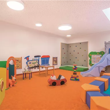 A colorful playroom with various toys and a slide. The walls are designed in bright colors and the floor is orange.