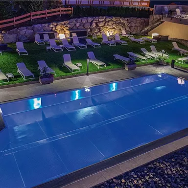 A modern pool surrounded by loungers and well-maintained lawn. The scene is illuminated in the evening and radiates a relaxed atmosphere.