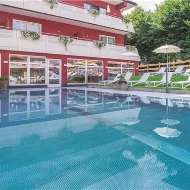 A quiet pool area with loungers and sun umbrellas. In the background, a modern building in red color can be seen.