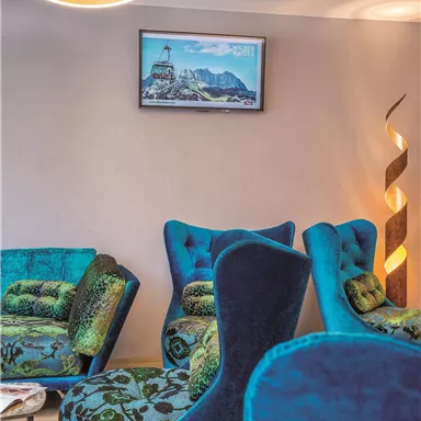 A modern living room with several blue armchairs and a unique chandelier. A picture of mountains and a city hangs on the wall.