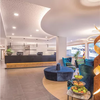 A modern reception hall with elegant furniture and bright walls. In the foreground, there is a round table with fruit and comfortable armchairs.