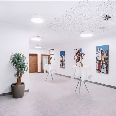 A modern room with bright, neutral design. Artworks hang on the wall and standing tables are placed in the room.