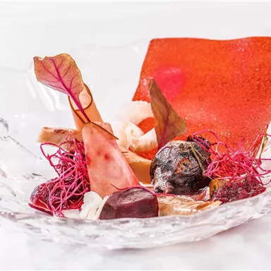 An artistic dish in a clear glass bowl. It showcases various ingredients, including colorful vegetables and creative decorations.