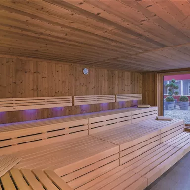 A tranquil sauna area made of wood with comfortable benches. Large windows provide a view of an outdoor area.