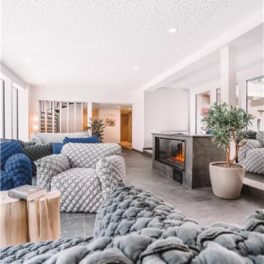 A modern living environment with cozy, woven armchairs and a fireplace. Large windows provide plenty of light and an inviting atmosphere.