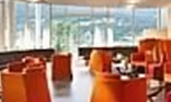 A modern café with stylish furniture in orange and red. Large windows offer a view of the surroundings.