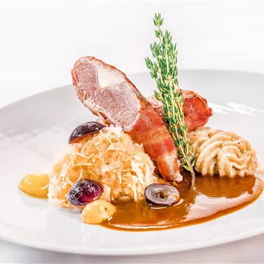 An artistically arranged plate with fried meat, side dishes of sauerkraut and pasta, as well as a sauce. Fresh herbs and some fruits complement the dish.
