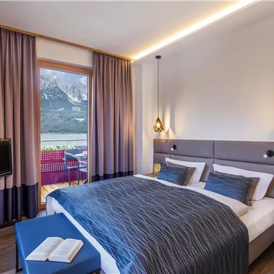 A modern hotel room with a large bed and cozy decoration. The window offers a beautiful view of the mountains.