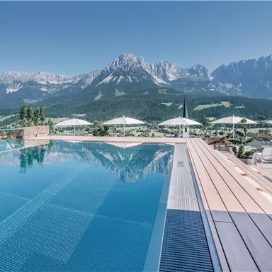 A beautiful infinity pool with a view of the mountains. The landscape is green and sunny, ideal for relaxing.