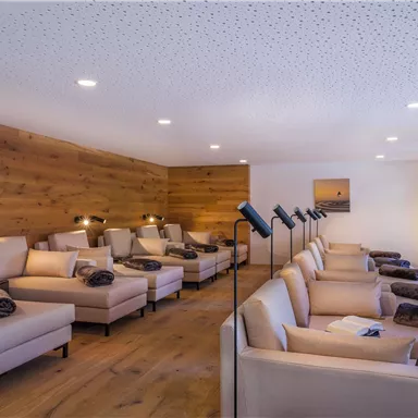 A cozy relaxation room with elegant loungers and warm wooden walls. The soft lighting creates a relaxing atmosphere.