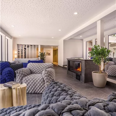 A modern living room with cozy gray and blue seating. The room features an elegant fireplace and large windows that let in plenty of light.