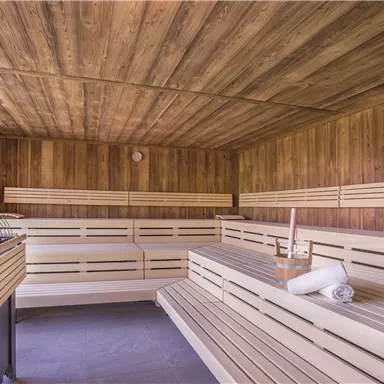 A modern sauna with wooden paneling and cozy benches. Large windows offer a view of nature.