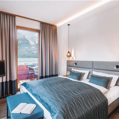 A modern hotel room with a large double bed and stylish decorations. The window offers a view of the mountains and a pleasant atmosphere.