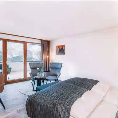 A modern hotel room with two beds and a desk. Large windows provide a beautiful view of the mountains.