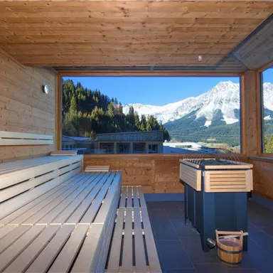 Ein schöner Saunabereich mit Holzbänken und einem Fenster, das auf schneebedeckte Berge blickt. Die Umgebung strahlt Ruhe und Entspannung aus.