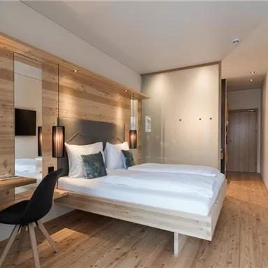 A modern bedroom with a wooden bed and elegant furnishings. Large windows provide plenty of light and a cozy atmosphere.