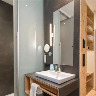 A modern bathroom with a glass shower and a stylish sink unit. The walls are done in dark and warm wood tones.