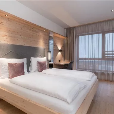 A modern bedroom with two single beds and wooden paneling. Large windows let in plenty of light and create a cozy atmosphere.