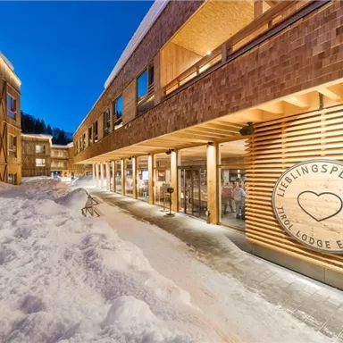 A modern lodge with wooden cladding and snow-covered ground. The clear evening sky gives the scene a cozy atmosphere.