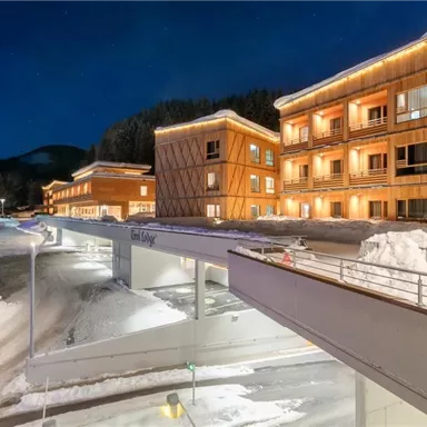 A modern building in the snow with warm light and a wooden facade. Surrounded by a tranquil winter landscape.