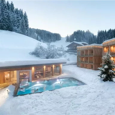 A hotel in a snow-covered landscape with an outdoor pool.  
Surrounded by snowy trees and mountains, it offers a cozy atmosphere.