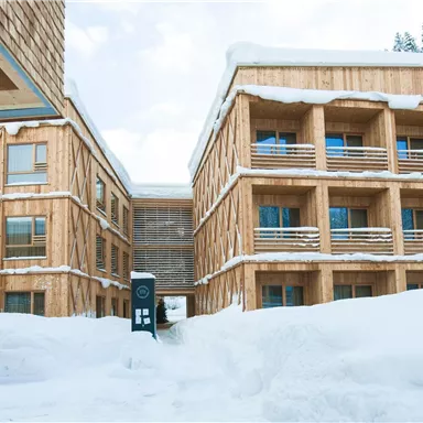 A modern wooden building in the snow, surrounded by a wintry landscape. The architecture is cozy and inviting, ideal for winter holidaymakers.
