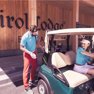 Ein Golfplatz mit einem Golfwagen und zwei Spielern. Im Hintergrund ist das Tirol Lodge-Schild zu sehen.