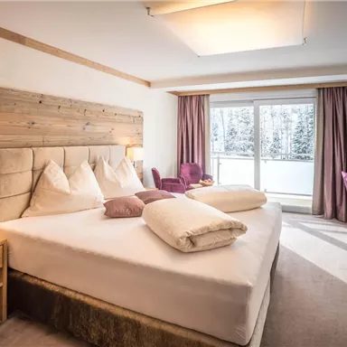 Ein modernes Schlafzimmer mit einem großen Bett und Holzdetails. Große Fenster bieten einen Blick auf die verschneite Landschaft.