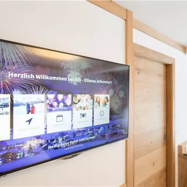 Ein moderner Fernseher in einem Hotelzimmer, der Informationen und Willkommensnachrichten anzeigt. Die Einrichtung ist klar und freundlich, mit einem hölzernen Design.
