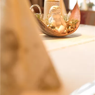 Ein schön gedeckter Tisch mit einer dekorativen Schale und einem kleinen Mädchen. Im Vordergrund sind gefaltete Servietten zu sehen.