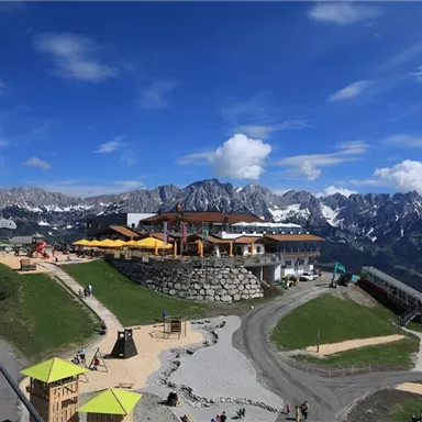 A picturesque mountain panorama with snow-capped peaks and a modern alpine inn. Surrounding the hut are hiking trails and leisure activities.