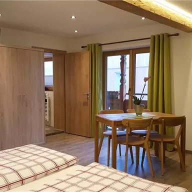 A cozy room with two beds, a table and chairs. Large windows with curtains and a TV on the wall.