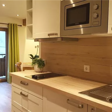 Modern kitchen with wooden elements and a window that looks out onto a balcony with a wooden railing. The kitchen is bright and friendly, featuring a plant arrangement on the countertop.