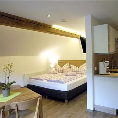 A cozy holiday apartment with a double bed, a small kitchen, and a dining area. Bright walls and wooden details create an inviting atmosphere.