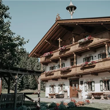 Ein traditionelles alpenländisches Haus mit einem Holzbalkon und bunten Blumen. Der Garten ist gut gepflegt und lädt zum Entspannen ein.