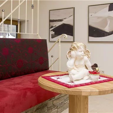 Ein gemütlicher Empfangsbereich mit einem roten Sofa und einer Holztafel. Auf der Tafel sitzt eine elegante Statue eines Engels.