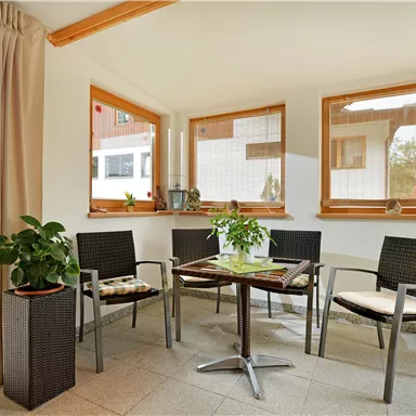 A bright and inviting room with large windows. There are chairs, a table, and some plants.