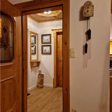 Ein einladender Eingangsbereich mit Holztüren und einem rustikalen Design. An der Wand hängen Bilder und eine klassische Uhr.