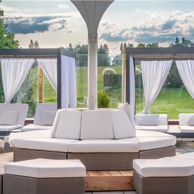 Ein eleganter Außenbereich mit gemütlichen Liegeflächen und weißen Drapierungen. Die grüne Landschaft im Hintergrund sorgt für eine entspannende Atmosphäre.