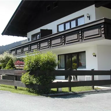 Ein schönes Haus im alpinen Stil mit einem schwarzen Balkongeländer. Der Garten ist gepflegt und die Umgebung ist von Bergen umgeben.