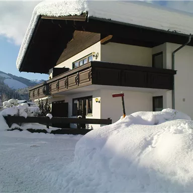 Ein charmantes Haus im Schnee mit einem überhängenden Dach. Die Umgebung ist winterlich und malerisch mit schneebedeckten Bäumen.