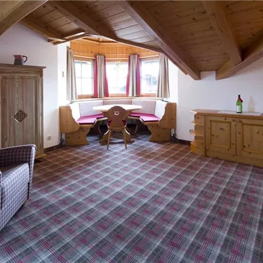 A cozy living space with a wooden ceiling and a seating area by the window. A comfortable corner with a table and a television completes the ambiance.