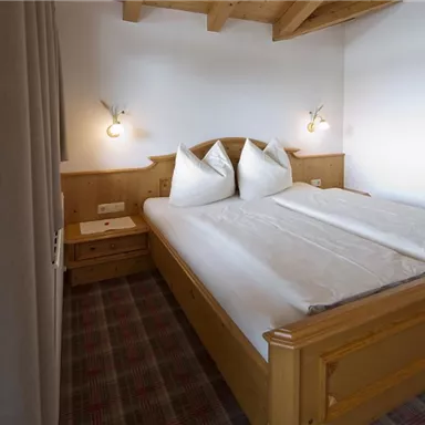 A cozy bedroom with a double bed and two large pillows. The wooden ceiling and soft lighting create an inviting atmosphere.