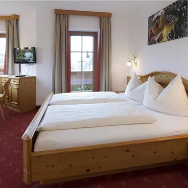 A cozy room with a double bed and wooden details. Large windows ensure plenty of light and a pleasant atmosphere.